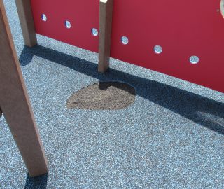 Playground surface damage prior to poured rubber repair.